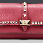 **Valentino Rockstud Wallet**: "Create an image of a luxurious Valentino Rockstud wallet made from fine calfskin leather, featuring iconic pyramid-shaped studs. The wallet should exude elegance and confidence, showcasing its practical interior with multiple card slots and a central compartment for bills. The background should reflect a chic and stylish environment."